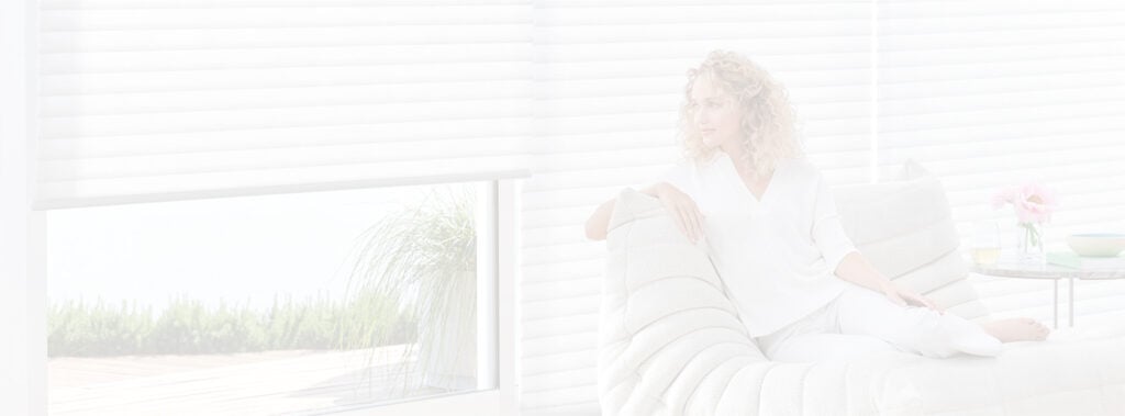 Woman relaxing on white couch by window blinds.