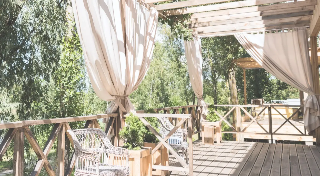 Sunny wooden patio with curtains and chairs.