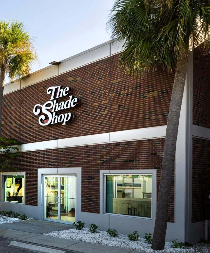 Brick building with 'The Shade Shop' sign, palm trees.
